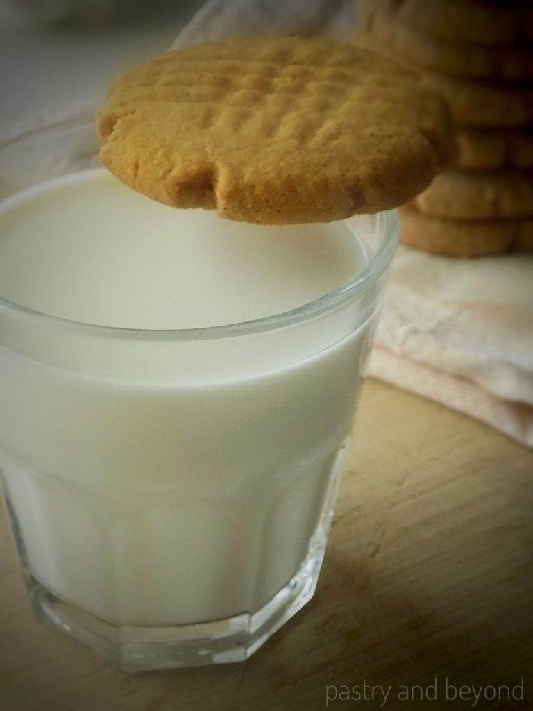 Cinnamon cookies on a glass of milk with the stacked cookies in the background.