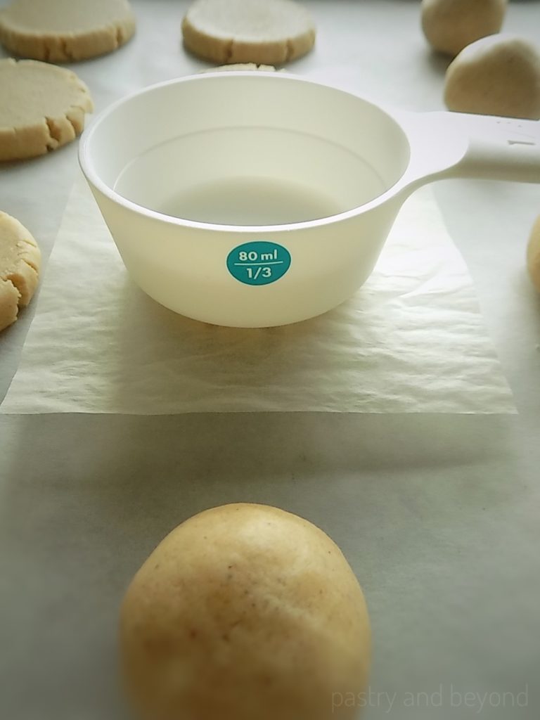 Flattening the cookie dough balls with a measuring cup.