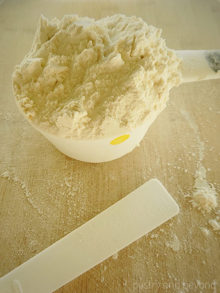 Measuring cup that is overfilled with flour, scraper on the front.