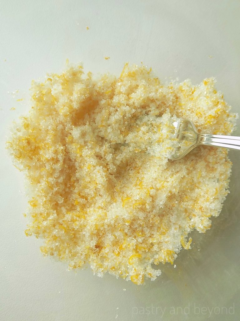 Sugar and lemon zest that are mixed in a bowl with a fork.