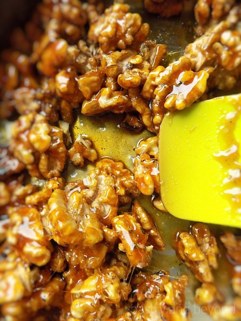 Mixing caramelized sugar with walnuts in a pan with a green spatula.