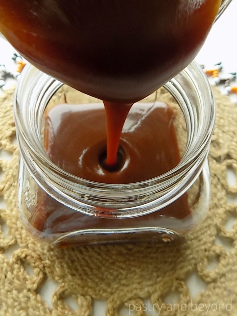 Pouring homemade caramel sauce from a pan into a jar.