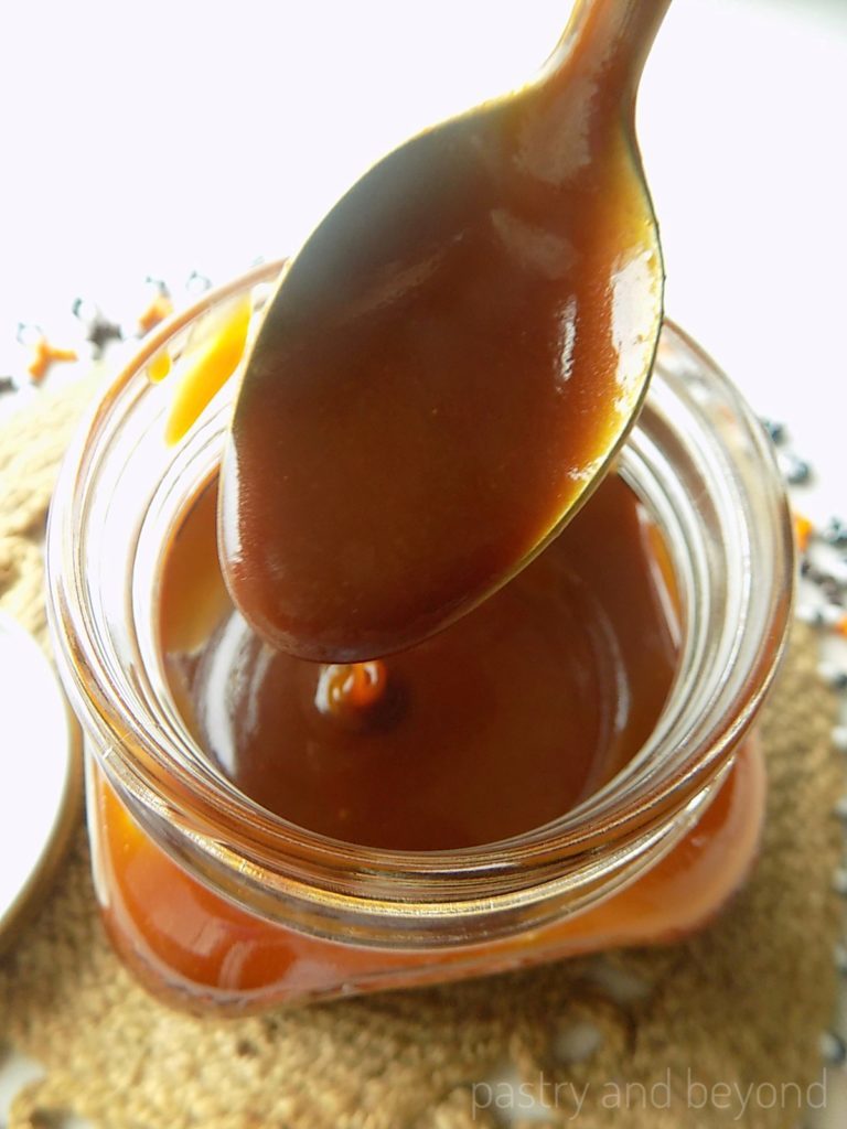 Caramel sauce is dripping from a spoon into a jar.