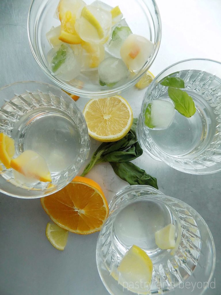 Fancy ice cubes with lemon, orange and basil leaves in glasses.