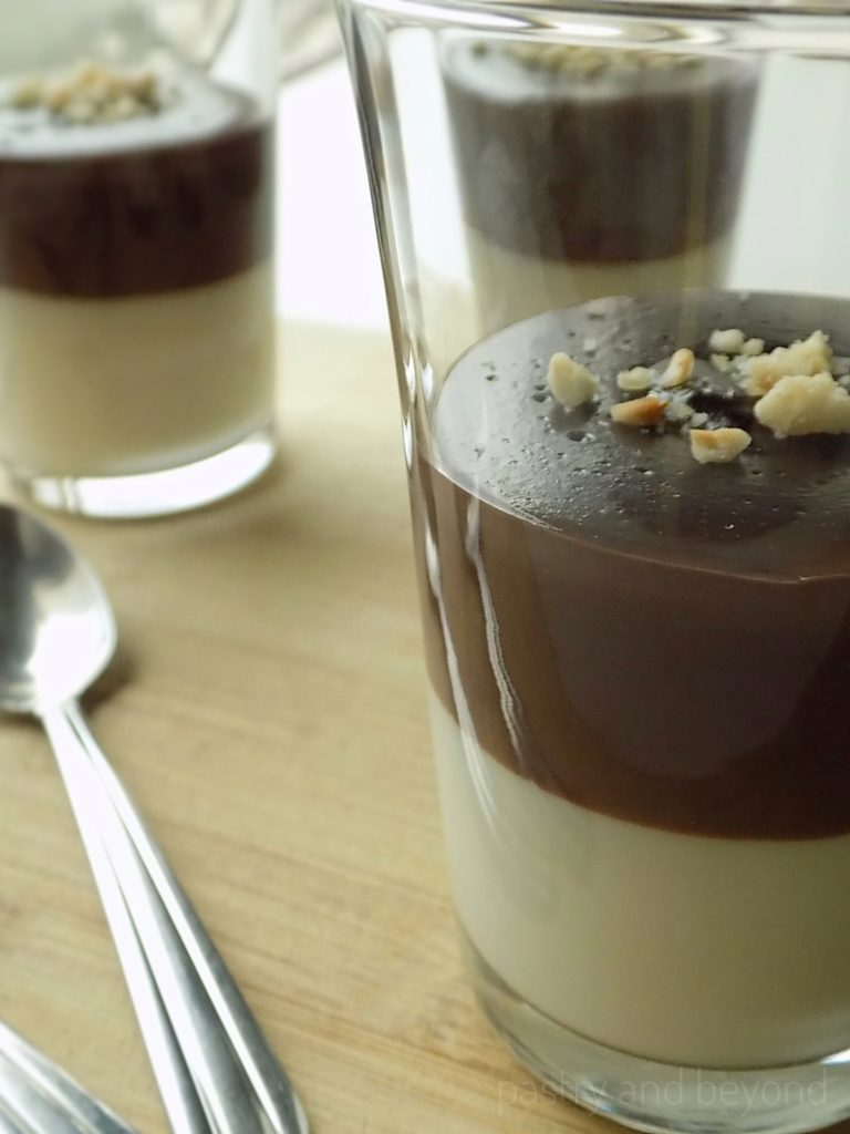 Two layer vanilla chocolate pudding in serving glasses on a wooden surface.