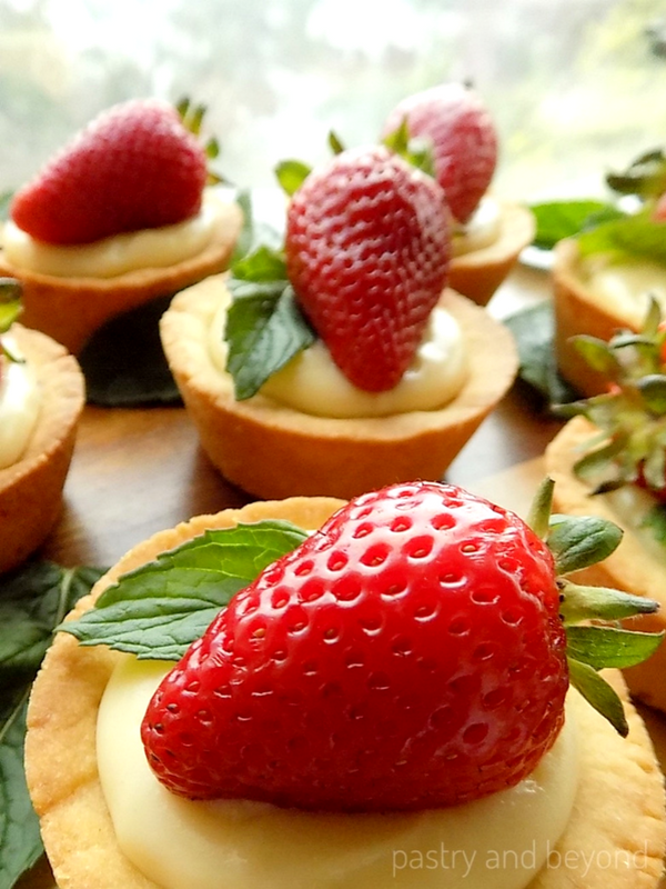 Cookie cups with strawberry, fresh mint and pastry cream on a wooden surface.