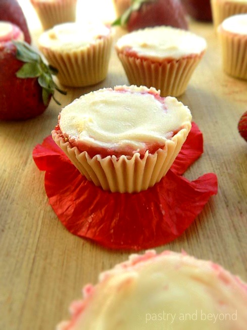 Frozen strawberry white chocolate cups with strawberries in the background.