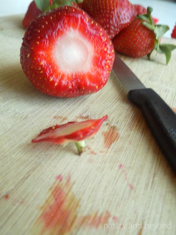 Stem removed strawberry on a chopping board with a knife and strawberries.
