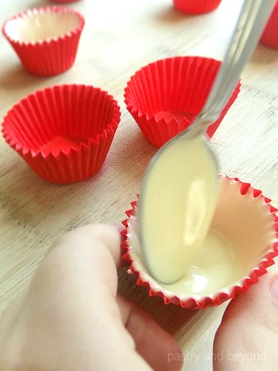 Covering the cupcake liners with melted white chocolate using a spoon.