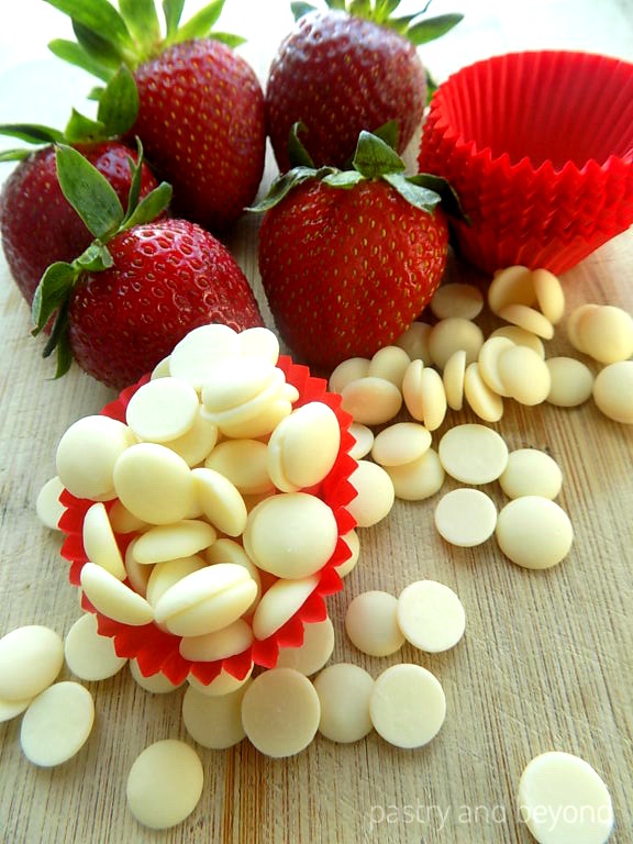 Strawberries, white chocolate and small cupcake liners on a wooden surface.