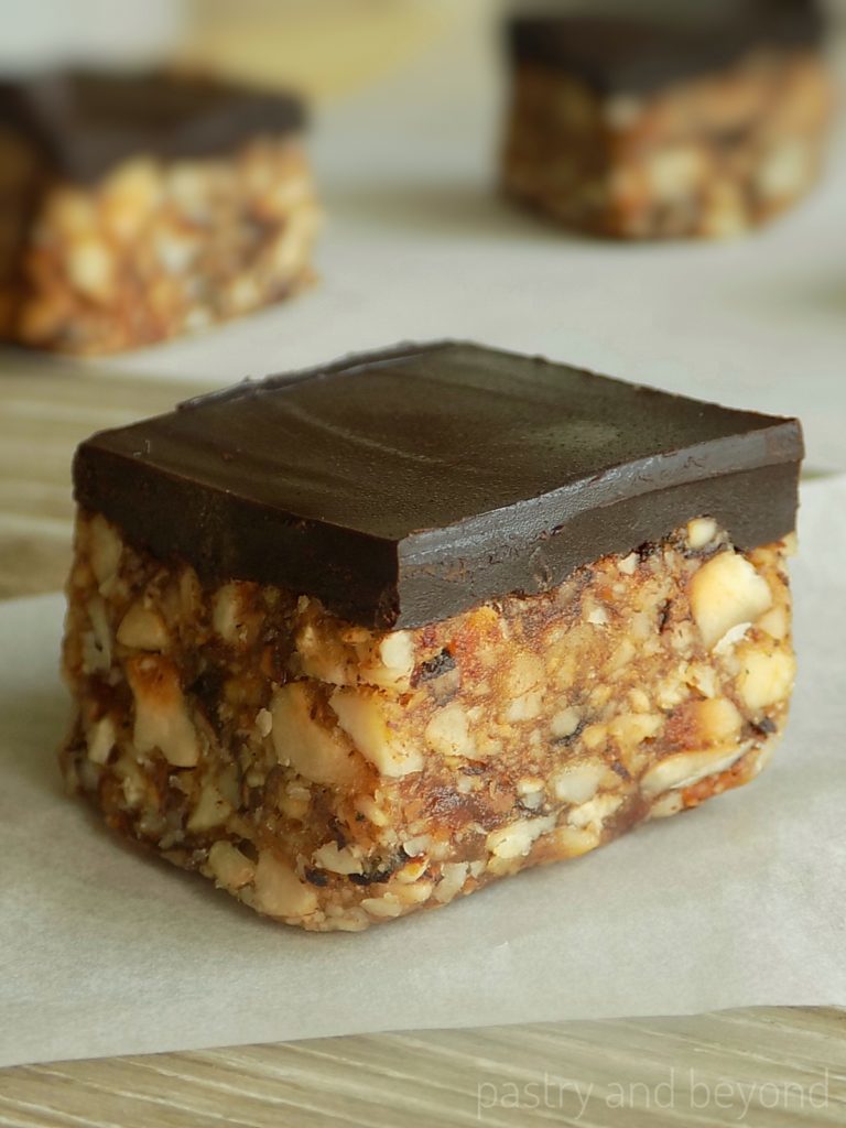 Chocolate covered date nut bars on a parchment paper that is placed on a wooden surface.