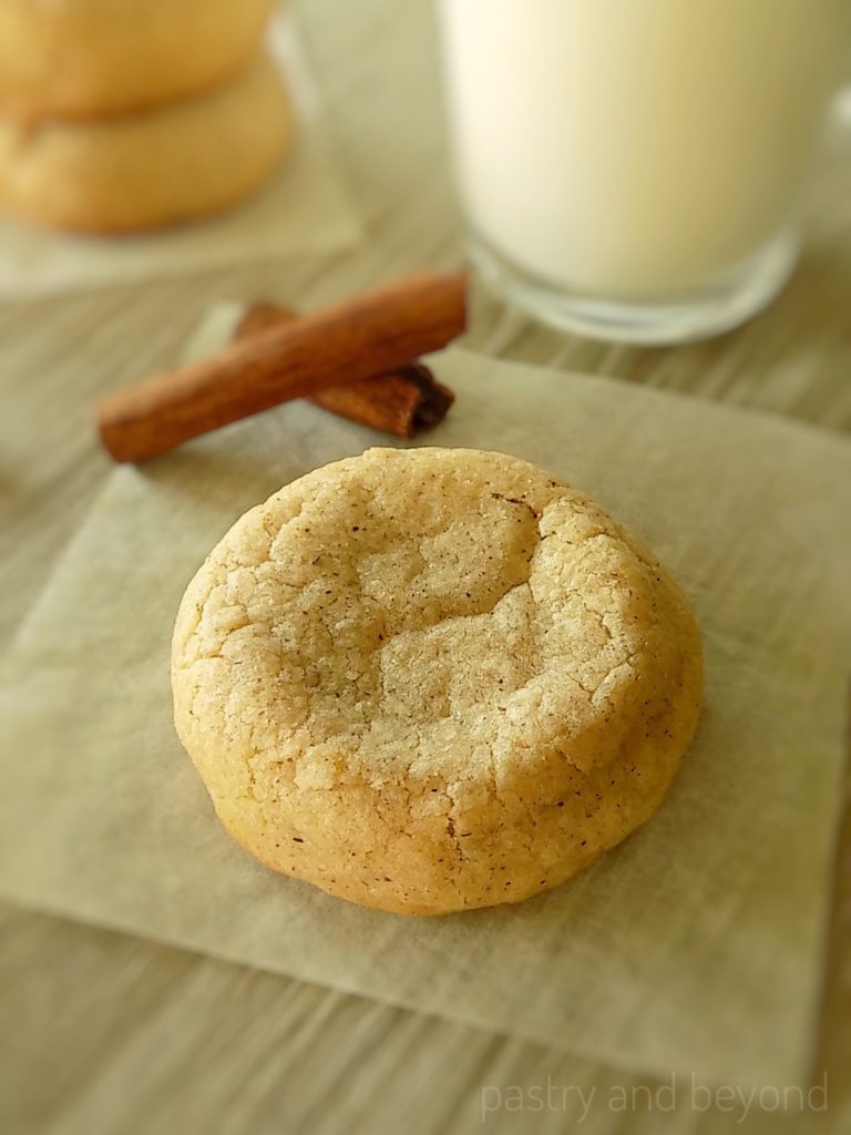 Cinnamon cookie with cinnamon sticks and a glass of milk in the background.