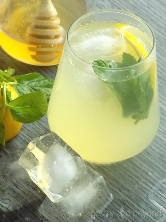 Single serve lemonade in a glass with a bottle of honey in the background.