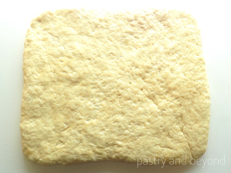 Soft bread roll dough is placed on a work surface as a rectangle.