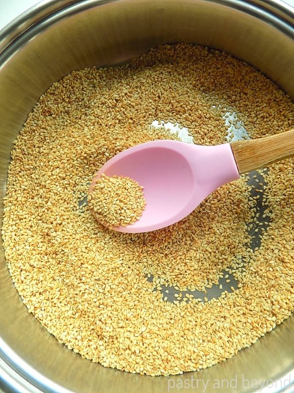 Toasted sesame seeds in a pan with a pink silicone spoon.