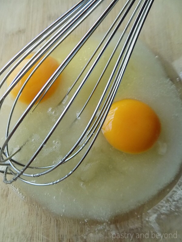 Sugar and eggs are in a mixing bowl with a whisk.