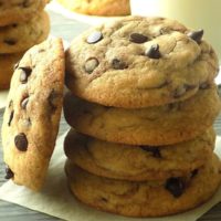 Stacked chocolate chip cookies on a parchment paper that is on a gray surface.