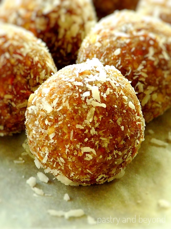 Almond date balls covered with shredded coconut on a white surface.