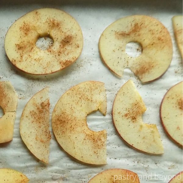 Thinly sliced apples with cinnamon on top on a baking sheet.