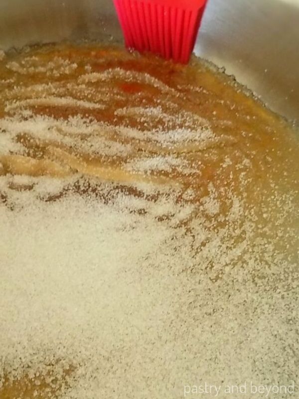 Step of making homemade caramel sauce; brushing down the sugar crystals that form on the sides of the pan. 