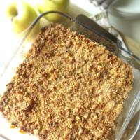 Overhead view of apple crumble in a baking dish with apples, plates, forks in the background.