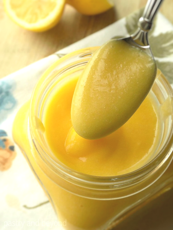 Homemade lemon curd on a spoon above the jar.