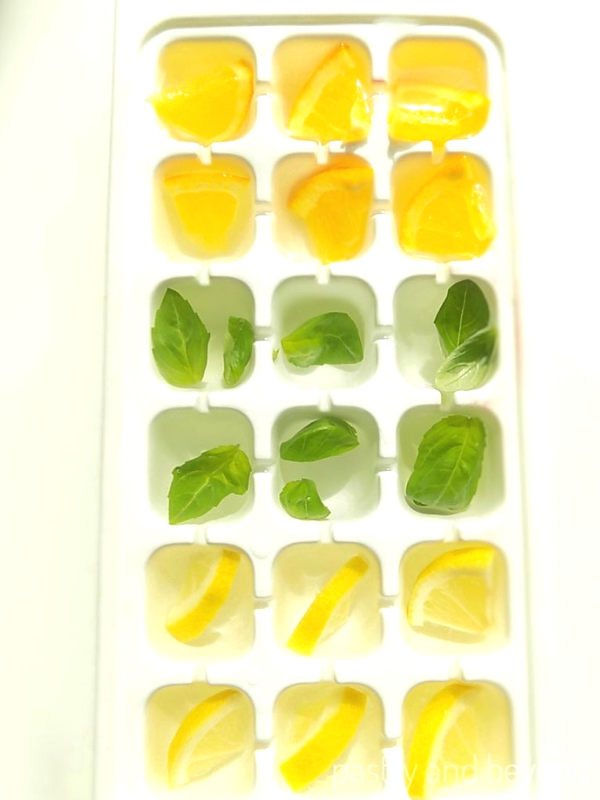 Ice tray filled with lemon, orange, basil leaves and water.