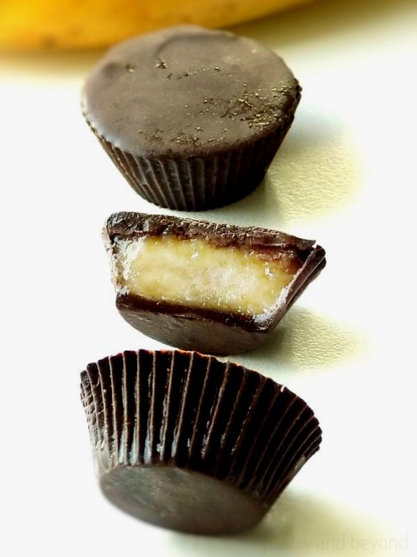 Frozen mashed bananas in dark chocolate cups on a white surface.