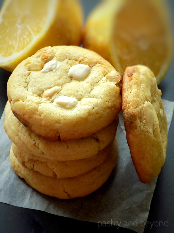 Stacked lemon white chocolate cookies, lemon cut in half in the background. 