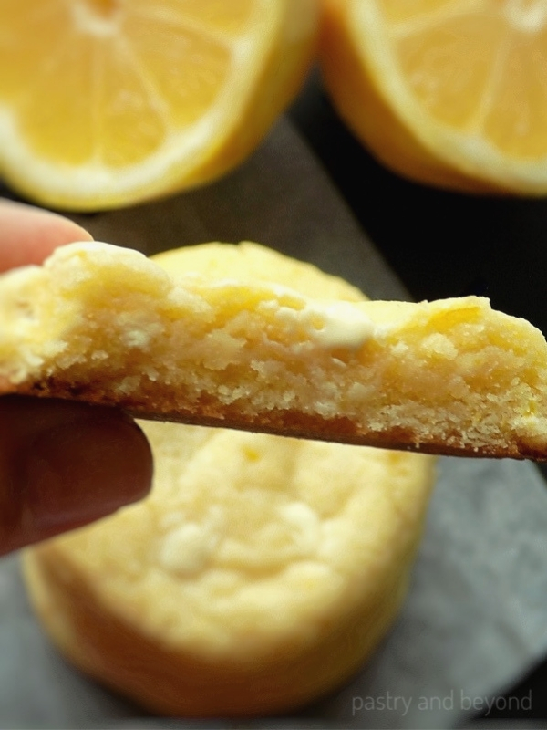 A hand holding half of the lemon and white chocolate cookie.