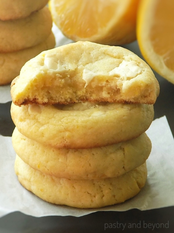 Stacked lemon white chocolate cookies, half of the cookie on top, lemons in the background.