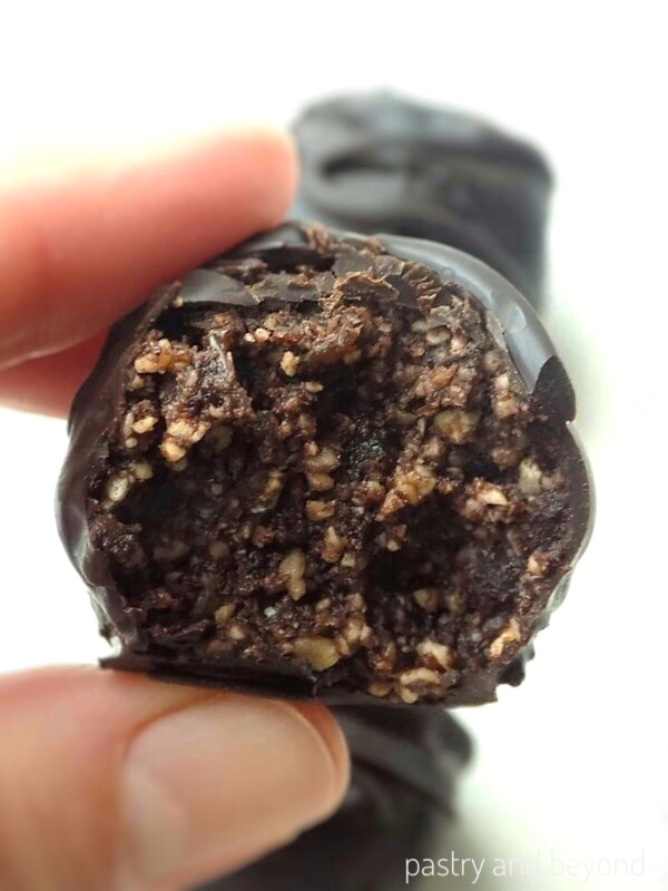 Holding half of the chocolate dipped raisin energy ball.
