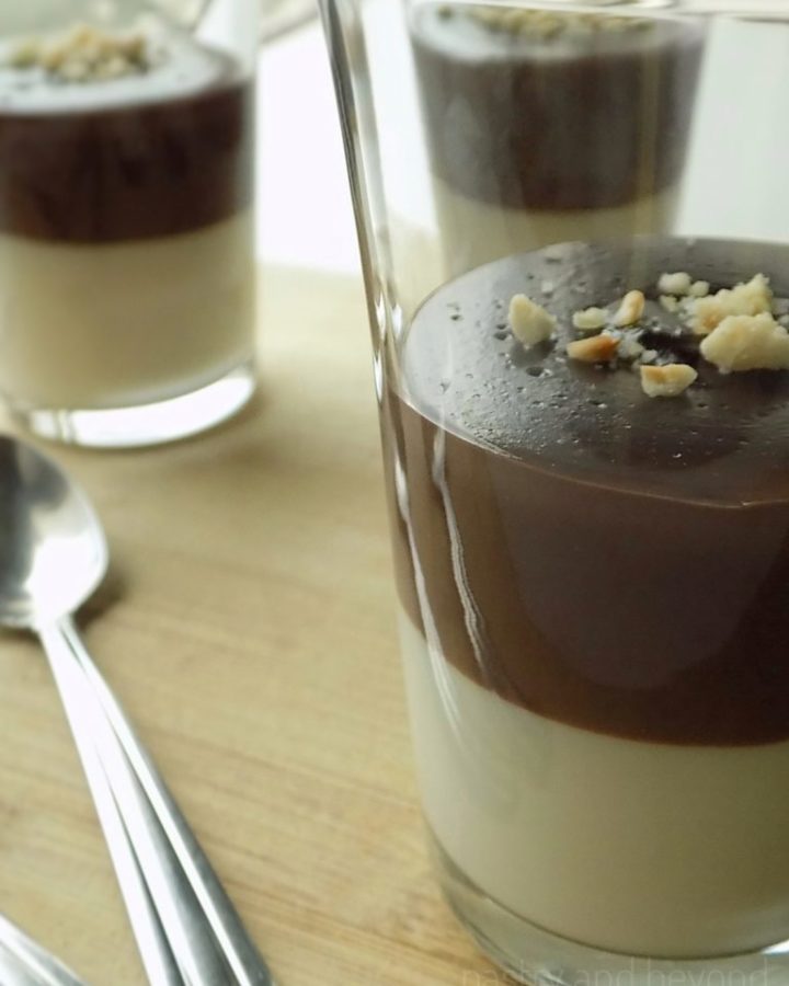 Two layer vanilla chocolate pudding in serving glasses on a wooden surface.