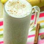 Banana smoothie with ground cinnamon on top and bananas in the background.