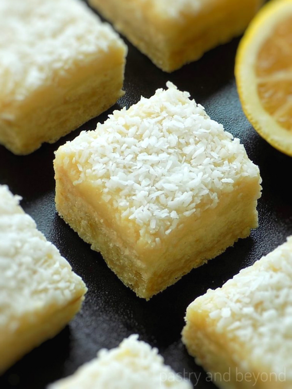 Lemon coconut bars on a black surface and a half lemon in the background.