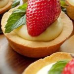 Cookies cups filled with pastry cream, topped with strawberry and mint.