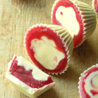 Frozen strawberry filled white chocolate cups on a wooden surface.