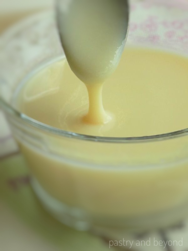 Homemade condensed milk pouring from a spoon which is thick after keeping in the fridge.