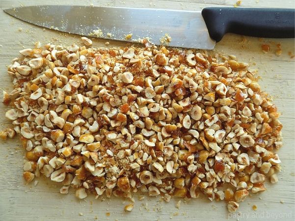 Chopped caramelized hazelnuts on a wooden board with a sharp knife.