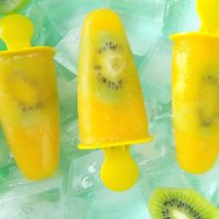 Orange popsicles with kiwi slices in a bowl that is full of ice cubes.
