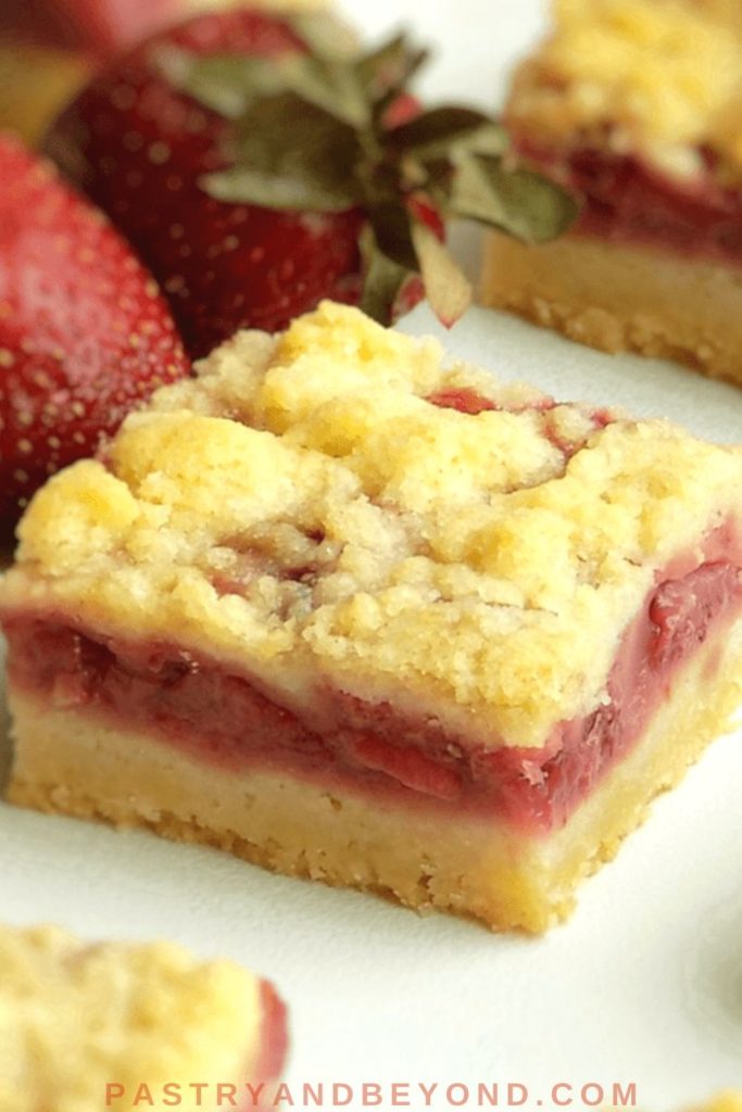 Strawberry Crumble bars on a white surface with strawberries on the background.
