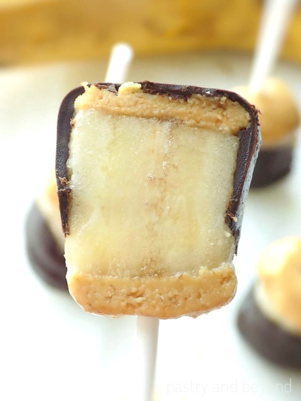 Half of the frozen banana covered with peanut butter and chocolate on a stick.