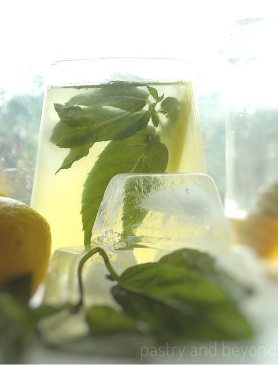 Lemonade in a glass with stacked ice cubes and mint leaves in front.