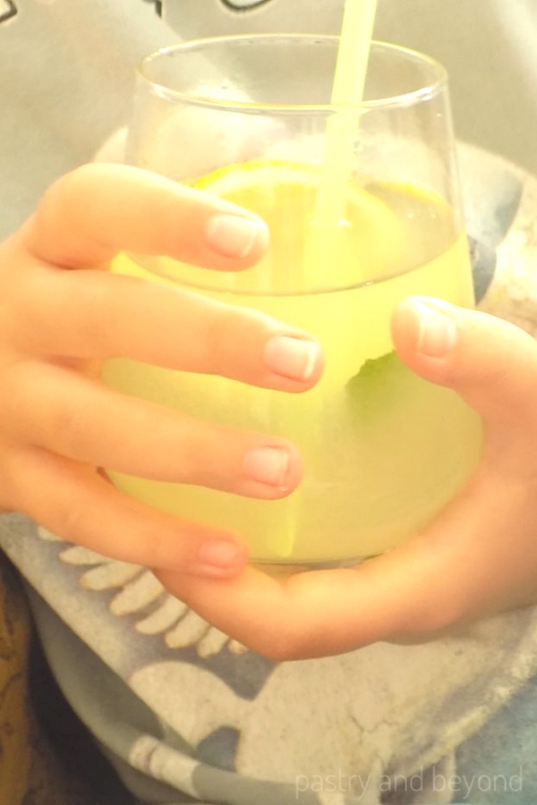 Holding a glass of lemonade with straw inside.