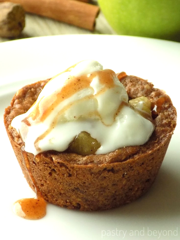 Apple crisp cookie cup topped with ice cream and syrup on a white plate.