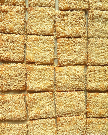 Small square sesame crackers on a parchment paper.