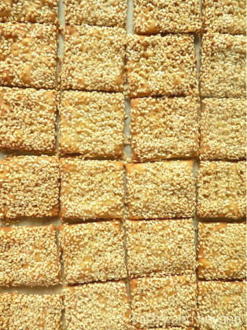 Small square sesame crackers on a parchment paper.