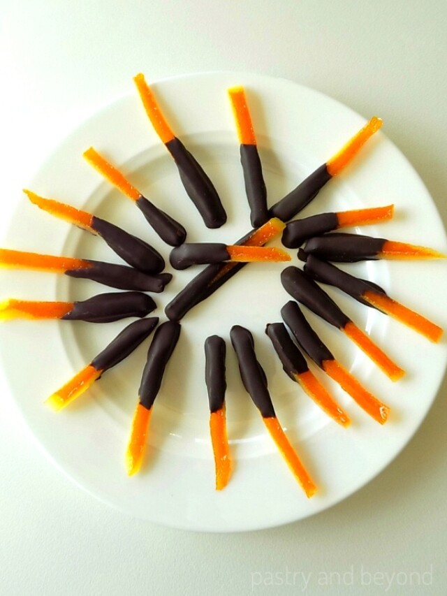 Chocolate dipped candied orange peels on a white plate.