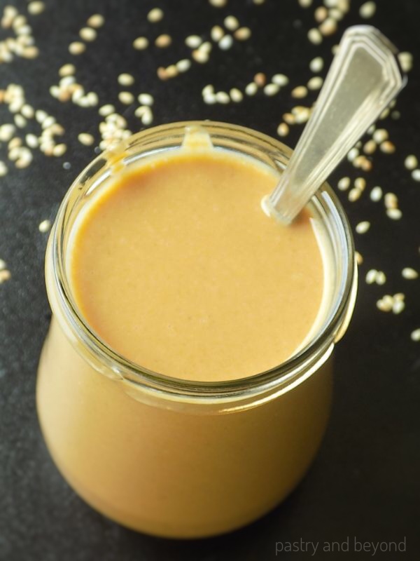 Tahini in a jar with a spoon inside on a black surface.