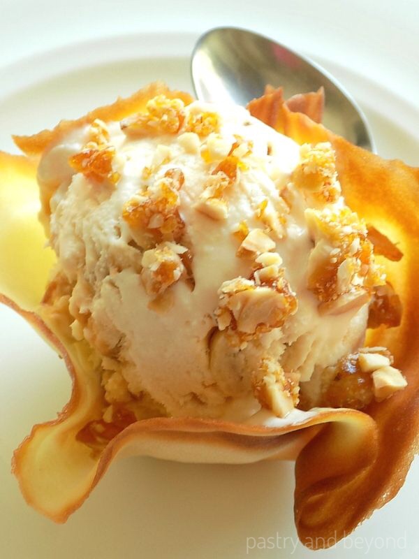 Praline ice cream in a tuile basket on a white plate with a spoon.